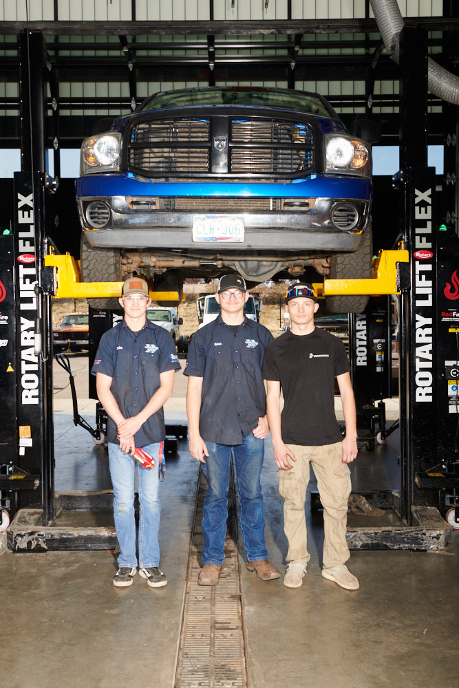 Automotive students pose for a portrait under a truck on a lift