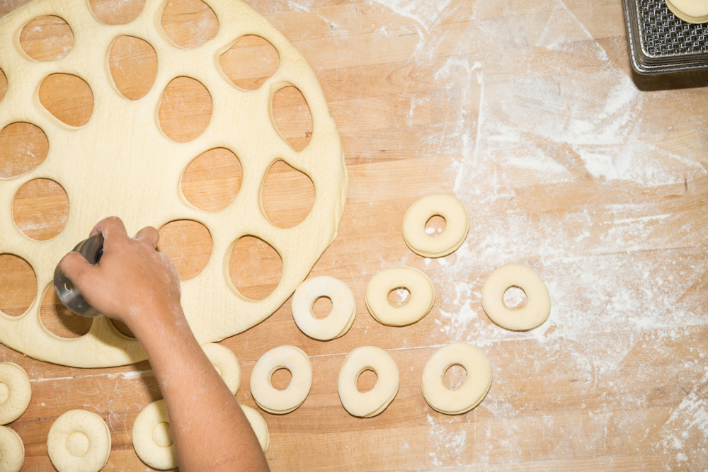 A baker's hand cutting donuts out of dough
