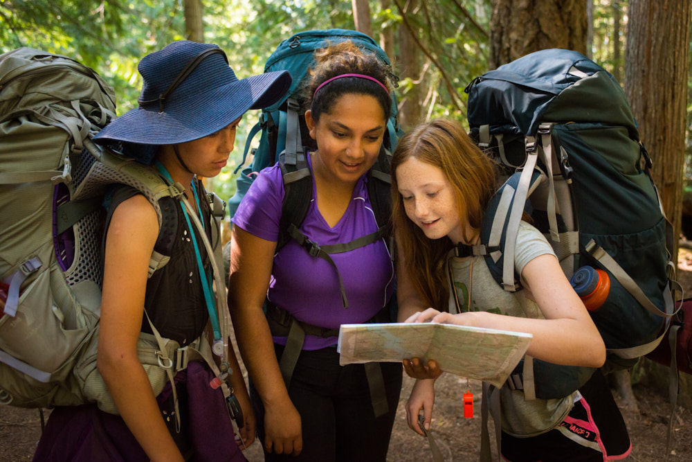 A counselor and two campers wearing backpacks examine a map