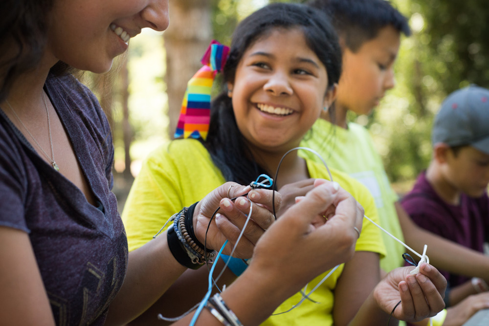 Smiling students make friendship bracelets with a counselor