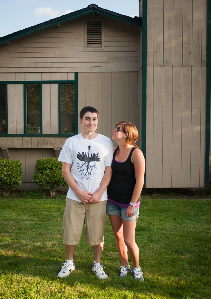 A couple standing for a portrait and smiling in front of a house