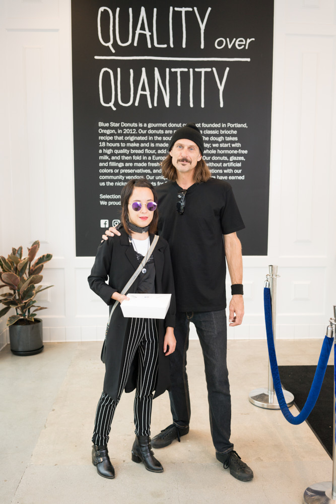 Two customers posing for a portrait in front of a Quality Over Quantity sign in a donut shop