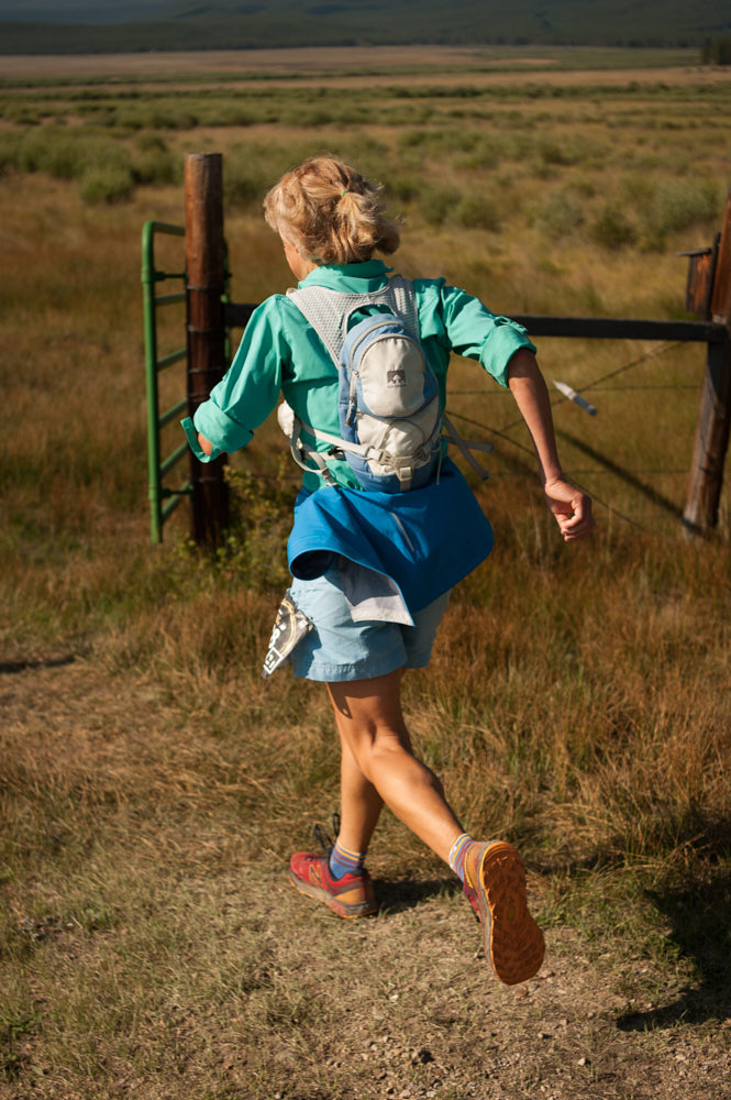 An elderly woman viewed from behind running with a backpack