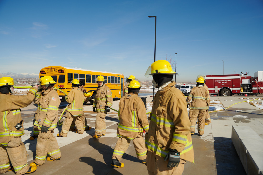 Firefighting students with a school bus and fire truck behind them