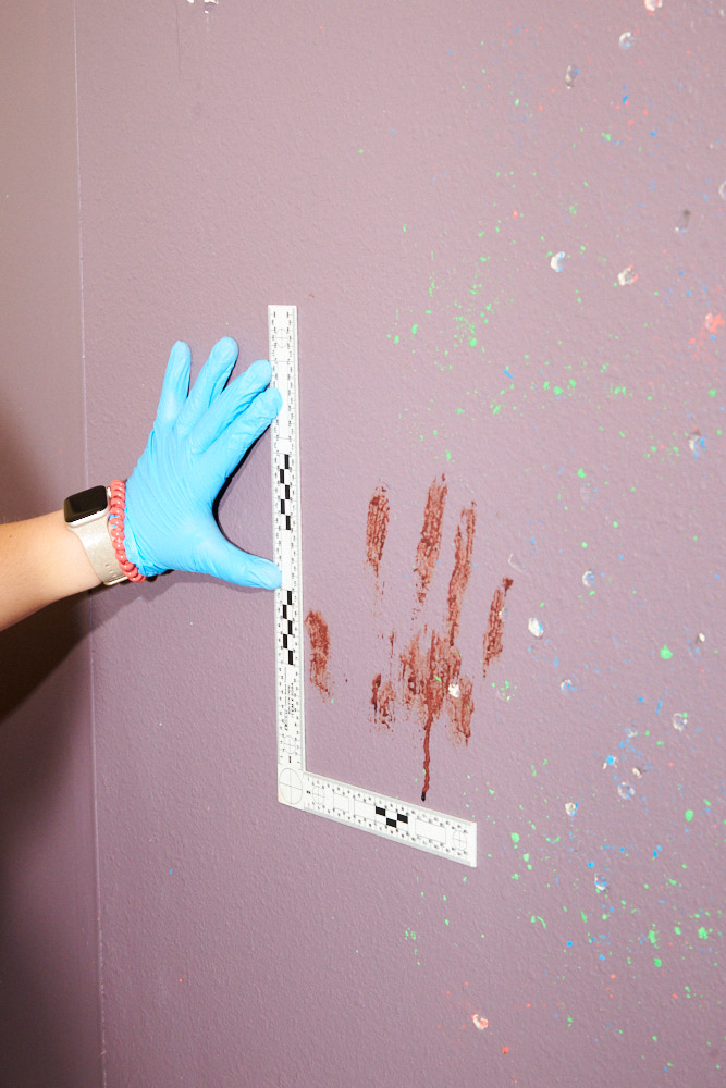 A gloved hand measuring a blood spatter during a forensics class