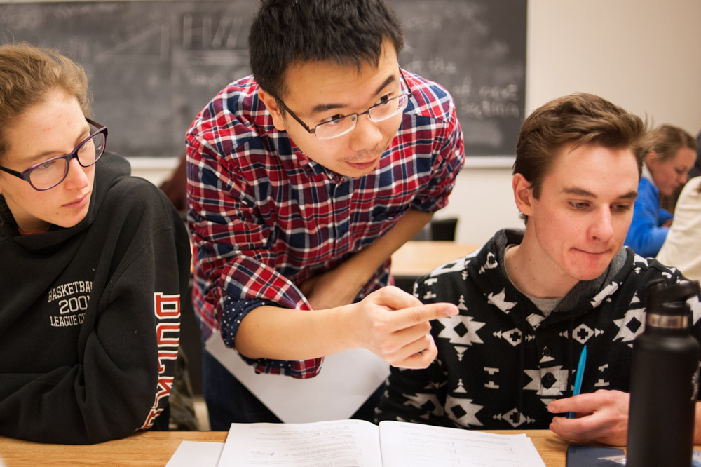 A TA talks and gestures with college students in a classroom