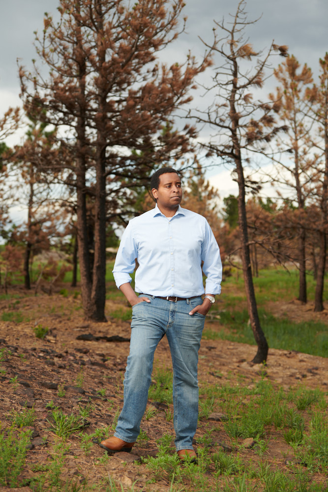 A portrait of congressman Joe Neguse near a wildfire burn