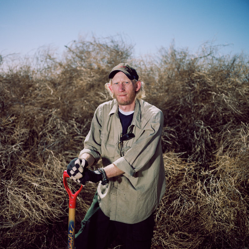 A man with a shovel in front of a pile of tumbleweeds