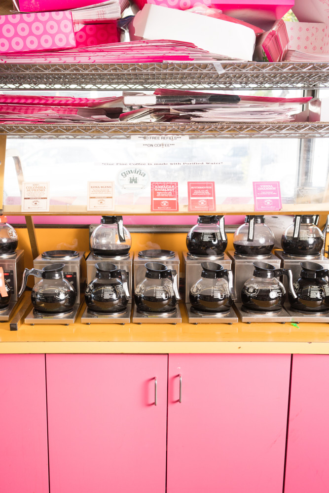 Many coffee pots on a pink and yellow cabinet