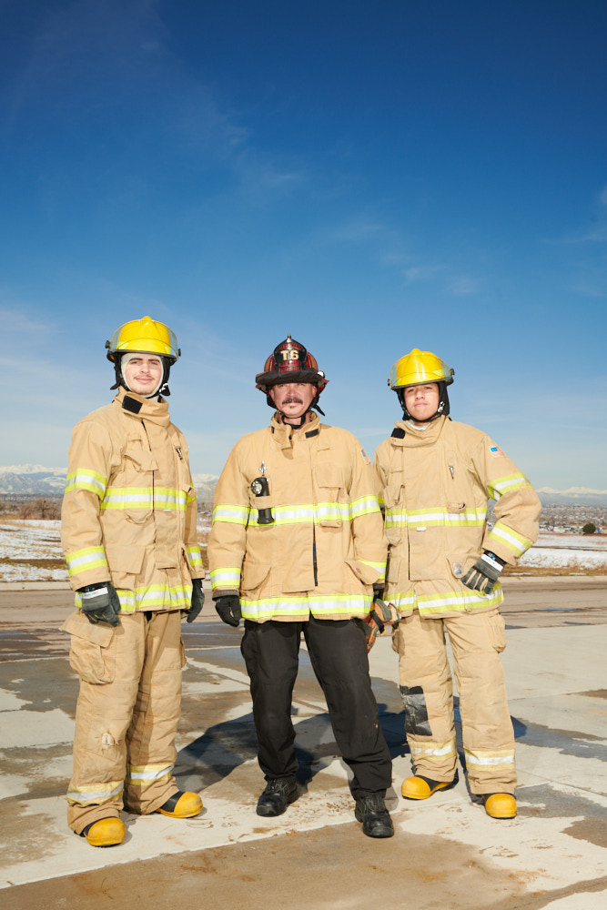 Two firefighting students stand in uniform with their teacher