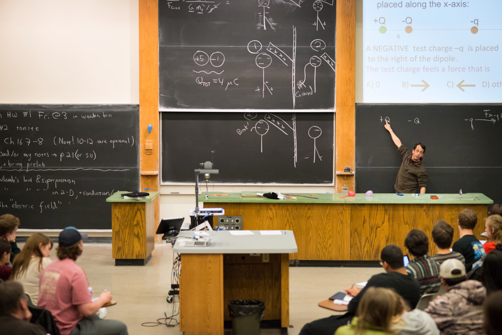 A professor teaching at a chalkboard in a lecture hall filled with students