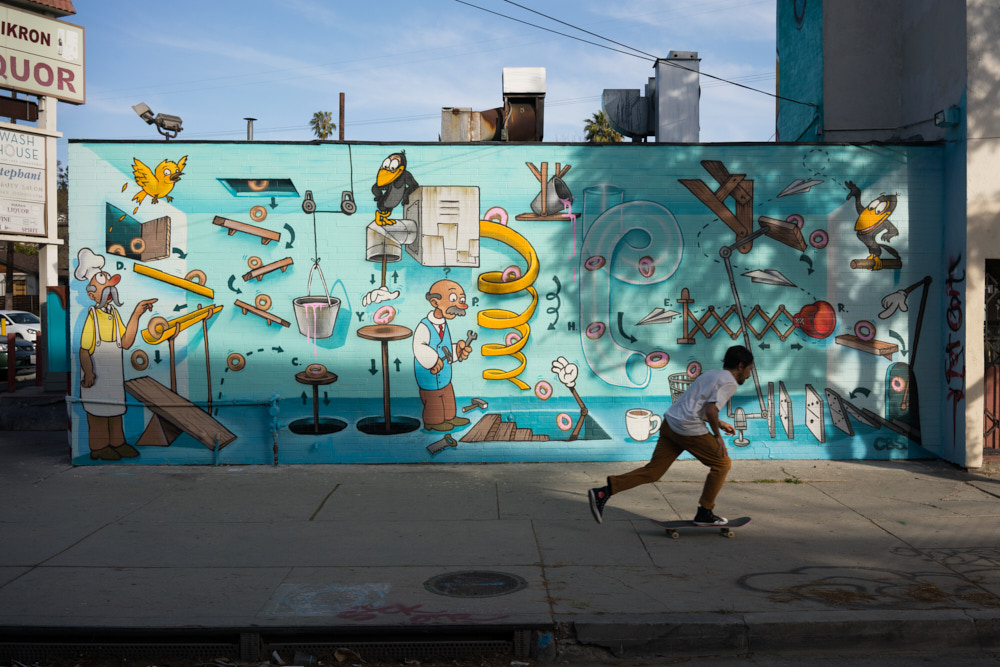 A skateboarder skates past a donut mural
