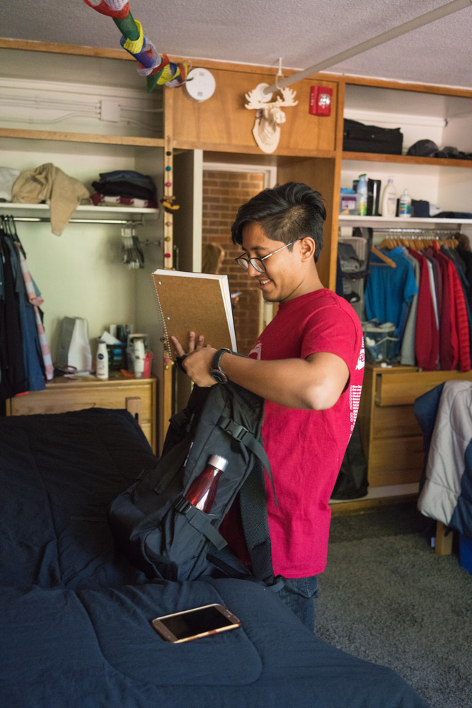 A student in his dorm room placing a notebook in his backpack