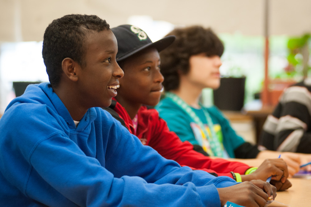 Students smile while sitting at a desk in a classroom