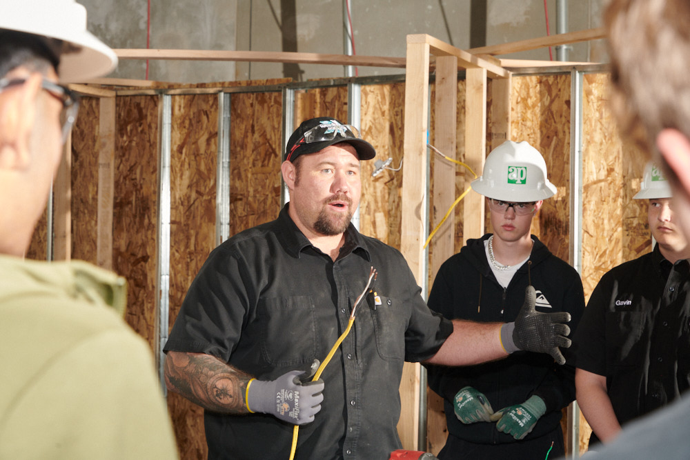 A teacher explaining wiring to students wearing hard hats