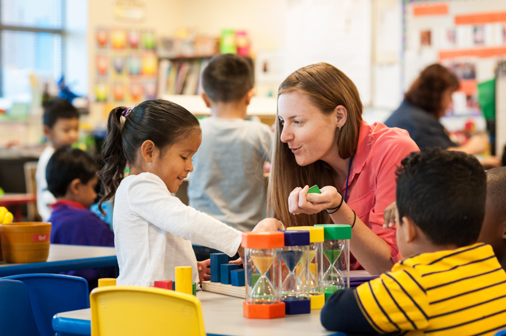 A teacher plays with toys next to a young student