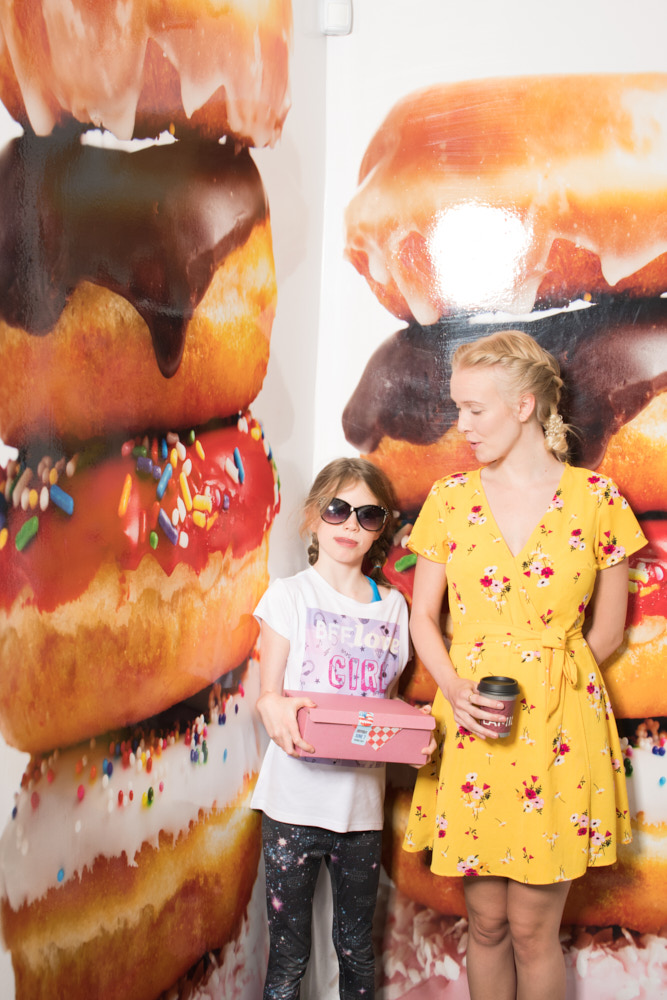 Two young women posing for a portrait in front of a wall adorned with giant photos of donuts
