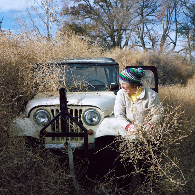 A woman clearing tumbleweeds off a Jeep