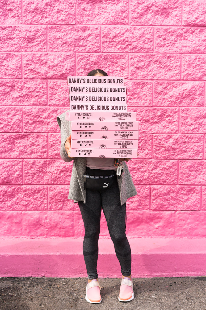 A portrait of a woman holding a stack of pink donuts boxes that covers her face