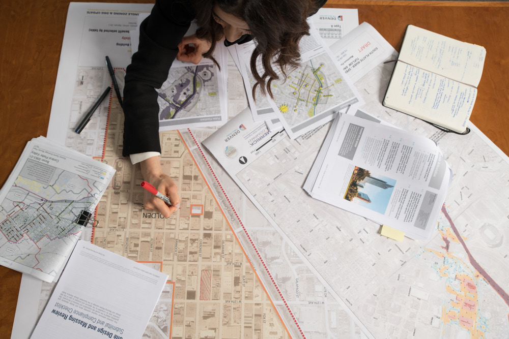 A woman viewed from overhead marks maps and paperwork at a desk