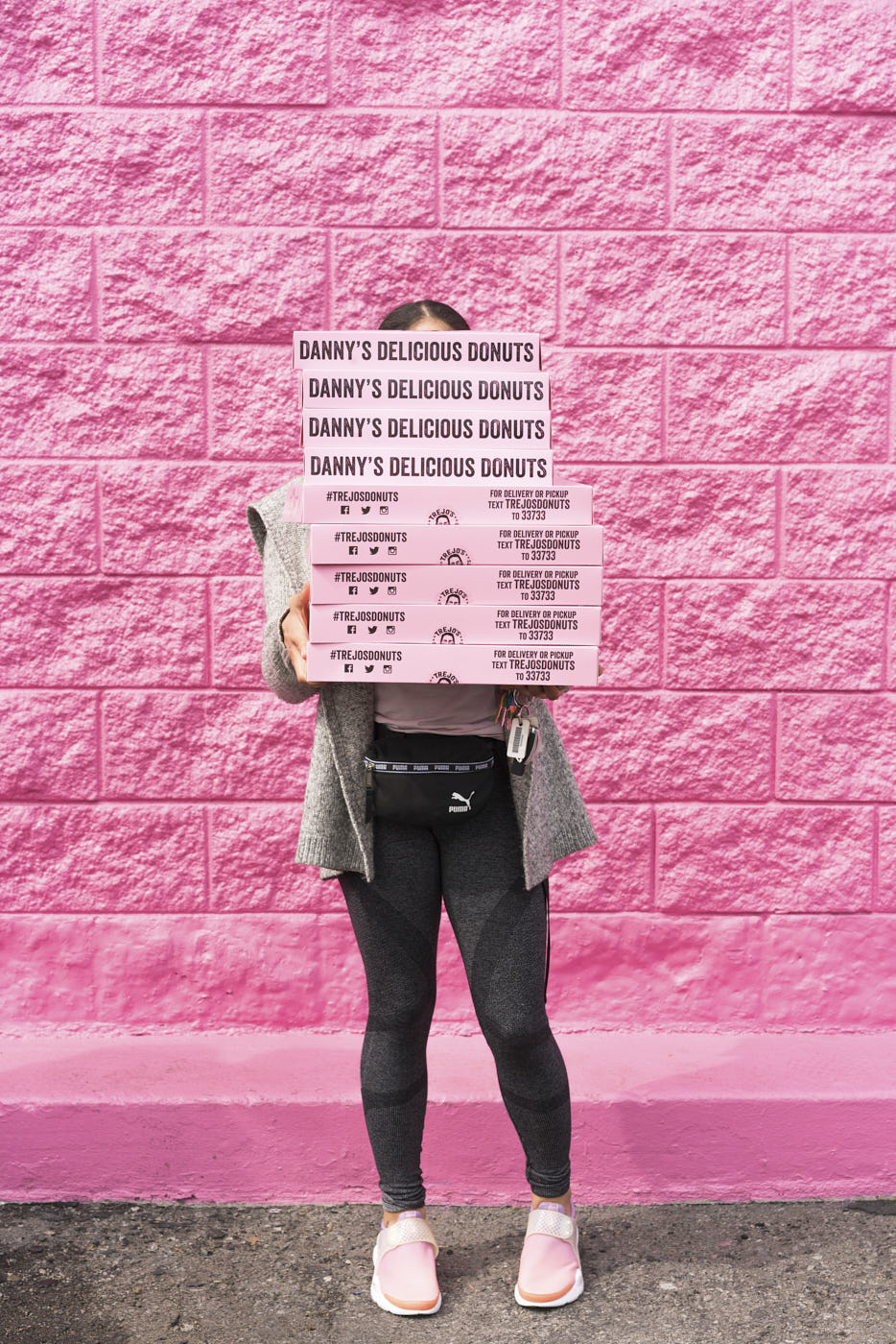 Woman holding pink donuts boxes against a pink wall